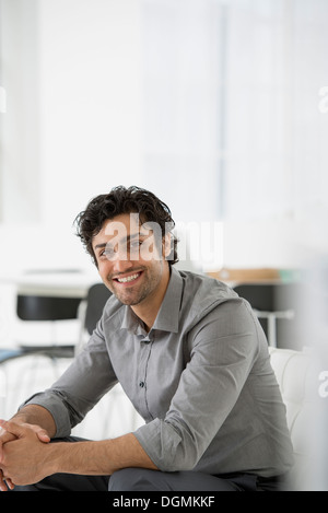 L'entreprise. Un homme assis avec ses mains jointes dans une atmosphère détendue. Sourire et se penchant en avant. Banque D'Images