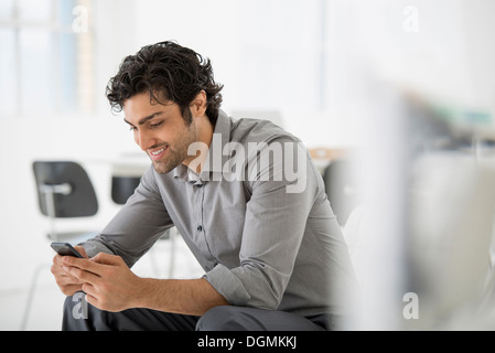 L'entreprise. Un homme assis à la recherche à l'écran sur son téléphone intelligent. Banque D'Images