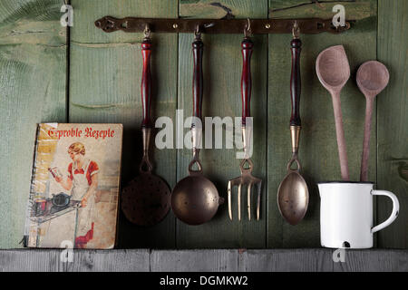 Ancien livre de cuisine et d'ustensiles de cuisine en face d'un mur en bois vert, Allemagne Banque D'Images