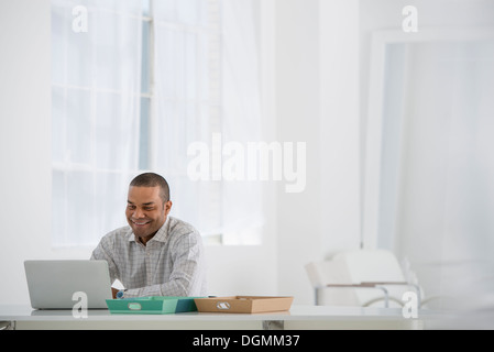 L'entreprise. Un homme assis à un bureau à l'aide d'un ordinateur portable. Banque D'Images