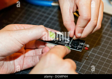 Les ongles peints avec la main et la main d'un enfant travaillant ensemble sur un appareil électronique avec des diodes électroluminescentes, IdeenPark, 2012 Banque D'Images