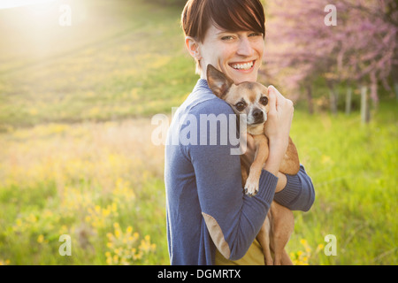 Une jeune femme dans les champs au printemps. Tenant un petit chihuahua chien dans ses bras. Un animal de compagnie. Banque D'Images