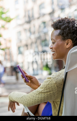 La vie en ville. Une femme assise dans un fauteuil de camping dans un parc de la ville, contrôle son téléphone cellulaire. Banque D'Images