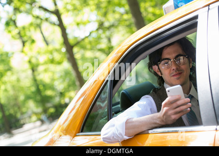 Un jeune homme sur le siège arrière d'un taxi jaune, regardant son téléphone intelligent. Banque D'Images