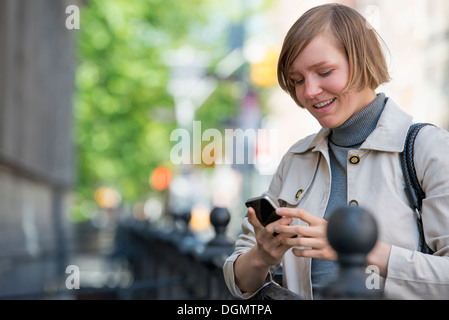 Ville. Une femme dans un contrôle de sa veste téléphone intelligent. Banque D'Images