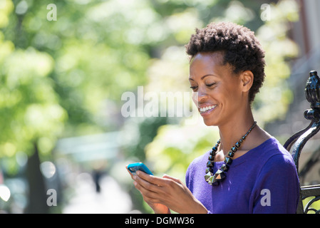 Ville. Une femme dans une robe pourpre contrôler son téléphone intelligent. Banque D'Images