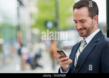 Ville. Un homme dans un costume d'affaires vérifier ses messages sur son téléphone intelligent. Banque D'Images