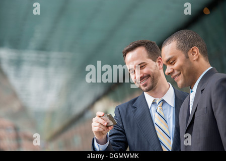 Ville. Deux hommes en costumes, regardant un smart phone, smiling. Banque D'Images