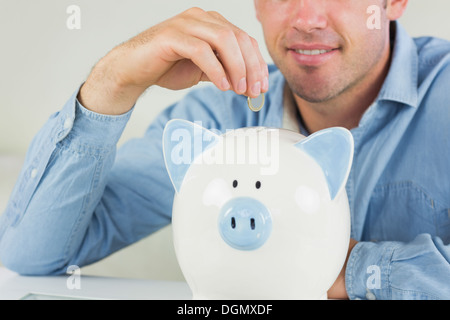 Happy casual man putting coins in piggy bank Banque D'Images