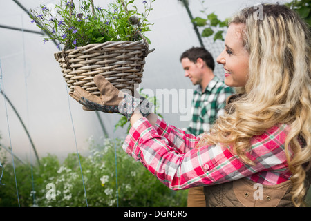 Belle femme touchant un panier de fleurs suspendus Banque D'Images