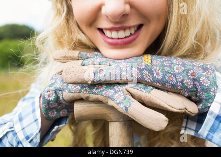 Cheerful blonde woman leaning on une pelle portant des gants de jardinage Banque D'Images