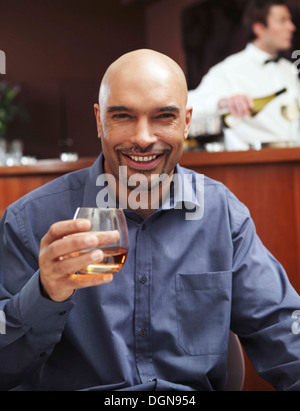 Un jeune homme assis dans un bar d'hôtel tenant un verre de brandy Banque D'Images