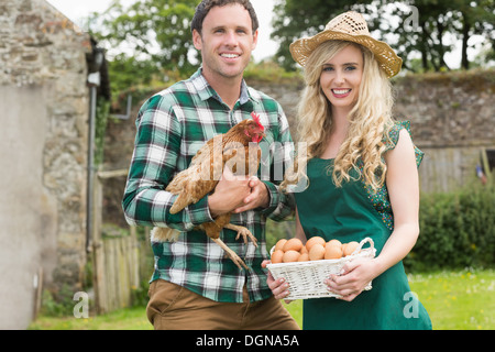 Smiling young couple holding chicken et panier d'œufs Banque D'Images