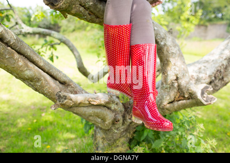 Femme portant des bottes en caoutchouc rouge assis sur un arbre Banque D'Images