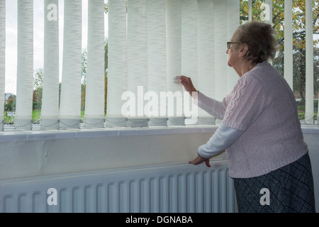 Femme de quatre-vingt-dix ans avec radiateur à la main regardant hors de la fenêtre. ROYAUME-UNI. Coronavirus, auto-isolation, distanciation sociale, quarantaine... concept Banque D'Images