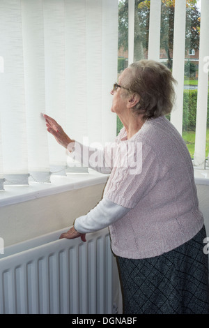 Femme de quatre-vingt-dix ans avec radiateur à la main regardant hors de la fenêtre. ROYAUME-UNI. Coronavirus, auto-isolement, distanciation sociale, quarantaine... concept Banque D'Images