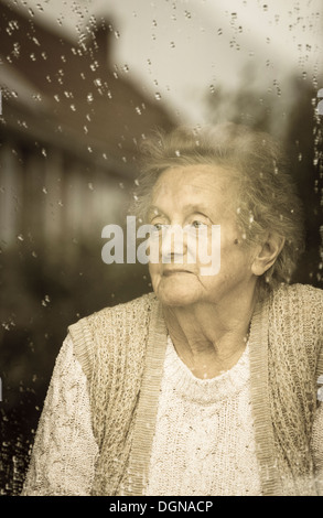 Femme de quatre-vingt-dix ans regardant hors de la fenêtre un jour de pluie. Auto isolement, quarantaine, Coronavirus, concept de distanciation sociale... Banque D'Images