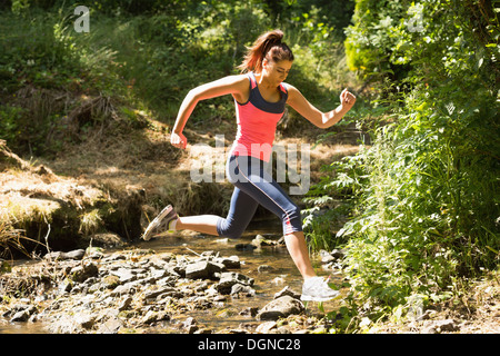 Jeune femme sportive sautant par-dessus un ruisseau Banque D'Images