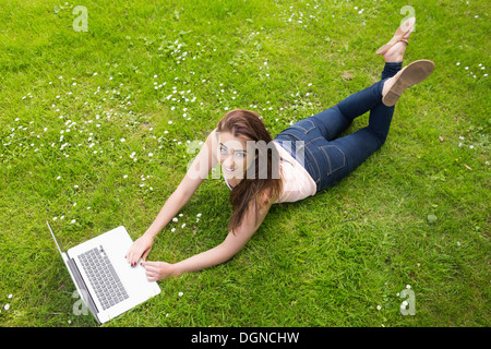 Happy young woman lying on a lawn en utilisant son ordinateur portable Banque D'Images