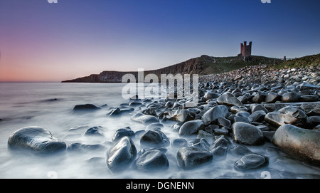 Plage de galets avec des ruines de château en arrière-plan Banque D'Images