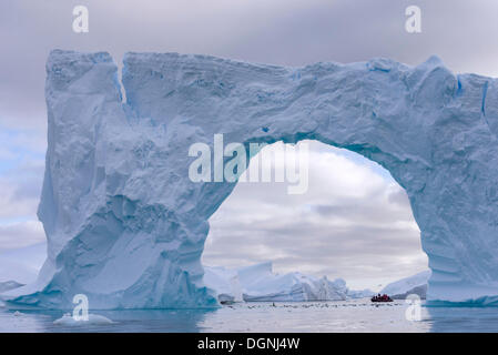 Bateau gonflable Zodiac vu à travers l'arche d'un grand iceberg, Pléneau Bay, péninsule Antarctique, l'Antarctique Banque D'Images