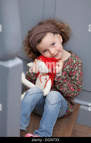 Fille aux cheveux roux, 5 ans, assis sur un escalier avec une poupée Banque D'Images