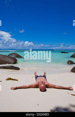 L'homme allongé sur une plage de l'anse dans le soleil, La Passe, l'île de Silhouette, les Seychelles, l'Afrique, de l'Océan Indien Banque D'Images