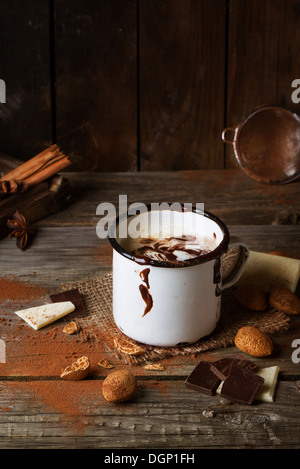 Mug vintage avec du chocolat chaud servi avec des morceaux de chocolat blanc et noir et d'amandes sur la vieille table en bois Banque D'Images