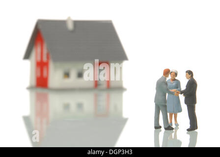 Couple qui achète une maison d'un agent immobilier, figurines, un flou chambre à l'arrière, image symbolique pour le marché de l'immobilier Banque D'Images
