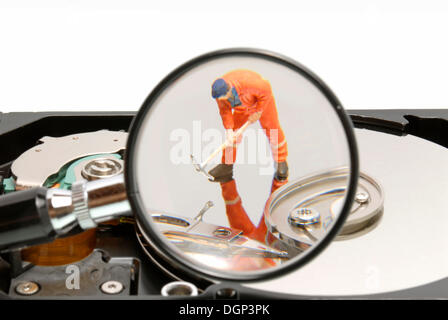 Petit travailleur de la construction figure sur un disque dur avec loupe, image symbolique pour le travail sur un support de données Banque D'Images