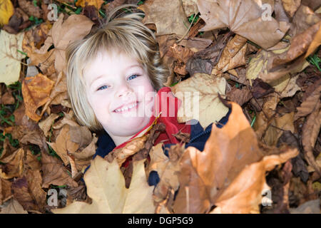 Petite fille, recouvert de feuilles d'automne dans un parc Banque D'Images