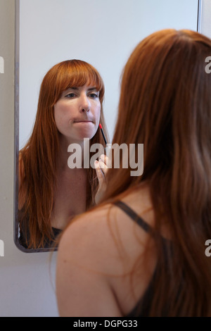 Mid adult woman applying lip gloss dans mirror Banque D'Images