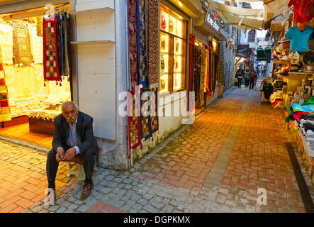 Homme assis à l'extérieur d'une boutique de tapis dans le bazar de Kusadasi, Kusadasi, Aydin province, région de l'Egée, la Turquie Banque D'Images