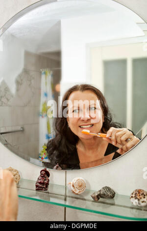 Femme se brosser les dents devant un miroir dans la salle de bains Banque D'Images