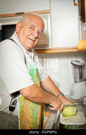 Homme âgé dans une cuisine salade de coupe Banque D'Images