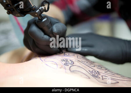 Mains d'un artiste de tatouage avec une machine à tatouer l'application d'un tatouage sur une épaule Banque D'Images
