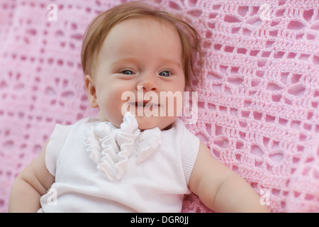 Sweet Little baby girl couché sur son dos vêtu d'un manteau blanc, regardant la caméra et rire de nouveau. Banque D'Images