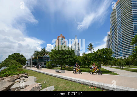 Couple riding vélos électriques, South Pointe Park, South Beach, Miami, Floride, USA Banque D'Images