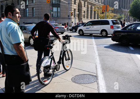 Homme tenant un vélo Bixi de voitures à un carrefour animé à Toronto, Ontario, Canada Banque D'Images