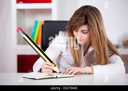 Businesswoman prenant des notes sur son bloc-notes avec un crayon géant Banque D'Images