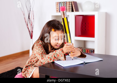 Petite fille à son domicile l'écriture avec un crayon géant Banque D'Images