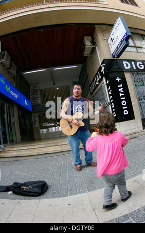 Une jeune fille qui marche au-delà d'un musicien de rue dans le village de Inca, dans l'île de Majorque, Espagne Banque D'Images