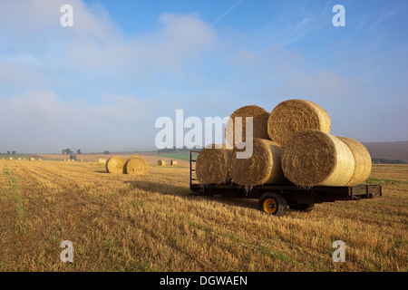 Un paysage avec une remorque de ferme avec des balles de paille rondes empilées dans un champ de chaume dans le Yorkshire Wolds Banque D'Images