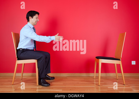 Poignée d'accord entre un homme et une chaise à côté d'un mur rouge Banque D'Images