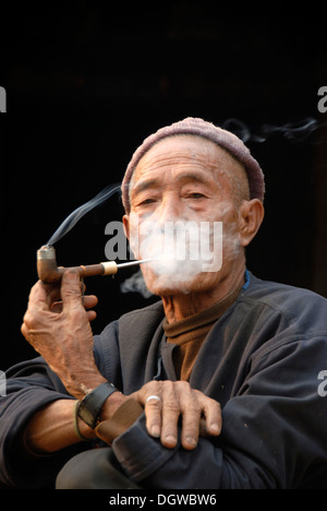 Portrait d'un vieil homme du groupe ethnique Mouchi fumant une pipe, la fumée couvrant son visage, pour le plaisir de fumer Banque D'Images