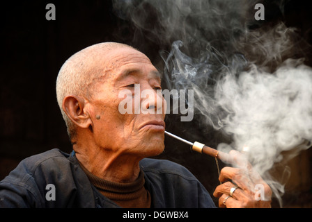 Portrait de profil d'un vieil homme du groupe ethnique Mouchi fumant une pipe, la fumée dans l'air, les village de Ban Mouchi Kang Banque D'Images