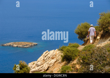 Femme de la randonnée le long d'un sentier raide falaise côtière, à la recherche sur une île et le bleu de la mer, en ordre décroissant de Moutti du Sotiras tis Banque D'Images