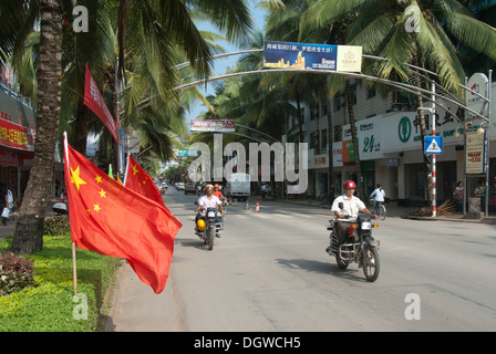 Drapeau national chinois, les cyclomoteurs équitation le long d'une avenue bordée de palmiers, Mengla, district autonome, Sipsongpanna Xishuangbanna Banque D'Images