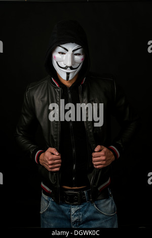 Jeune homme portant un masque anonyme avec un capuchon et une veste en cuir noir Banque D'Images