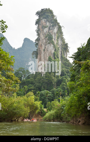 Les kayakistes de l'aviron sur une rivière à travers la jungle, avec un paysage karstique pinnacle rock s'élevant au-dessus de eux Banque D'Images